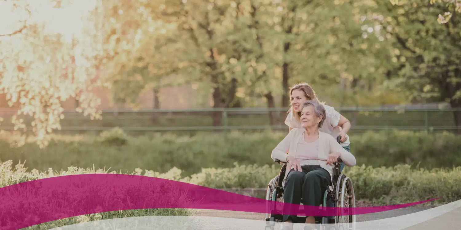 Woman pushing an elderly woman in a wheelchair along a path with trees in the background